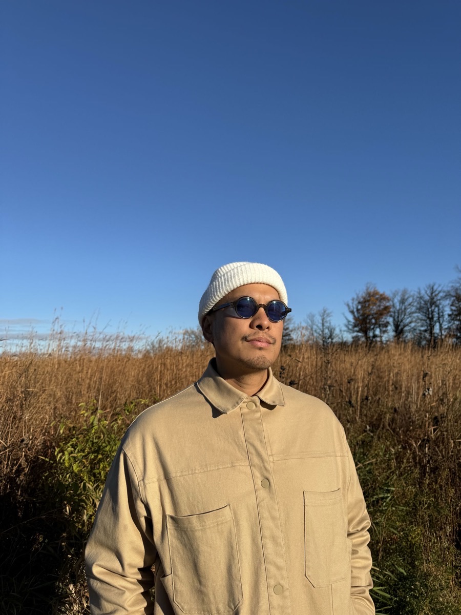 Portrait of Lex Junior outdoors in a beige jacket, beanie and sunglasses.